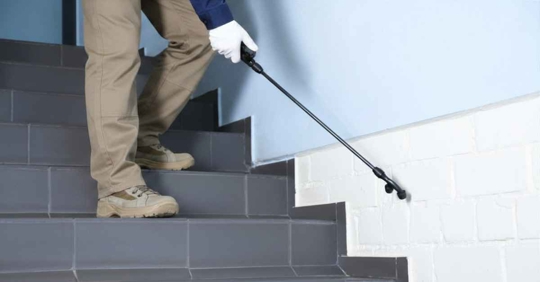 Pest control worker spraying pesticide on stairs indoors